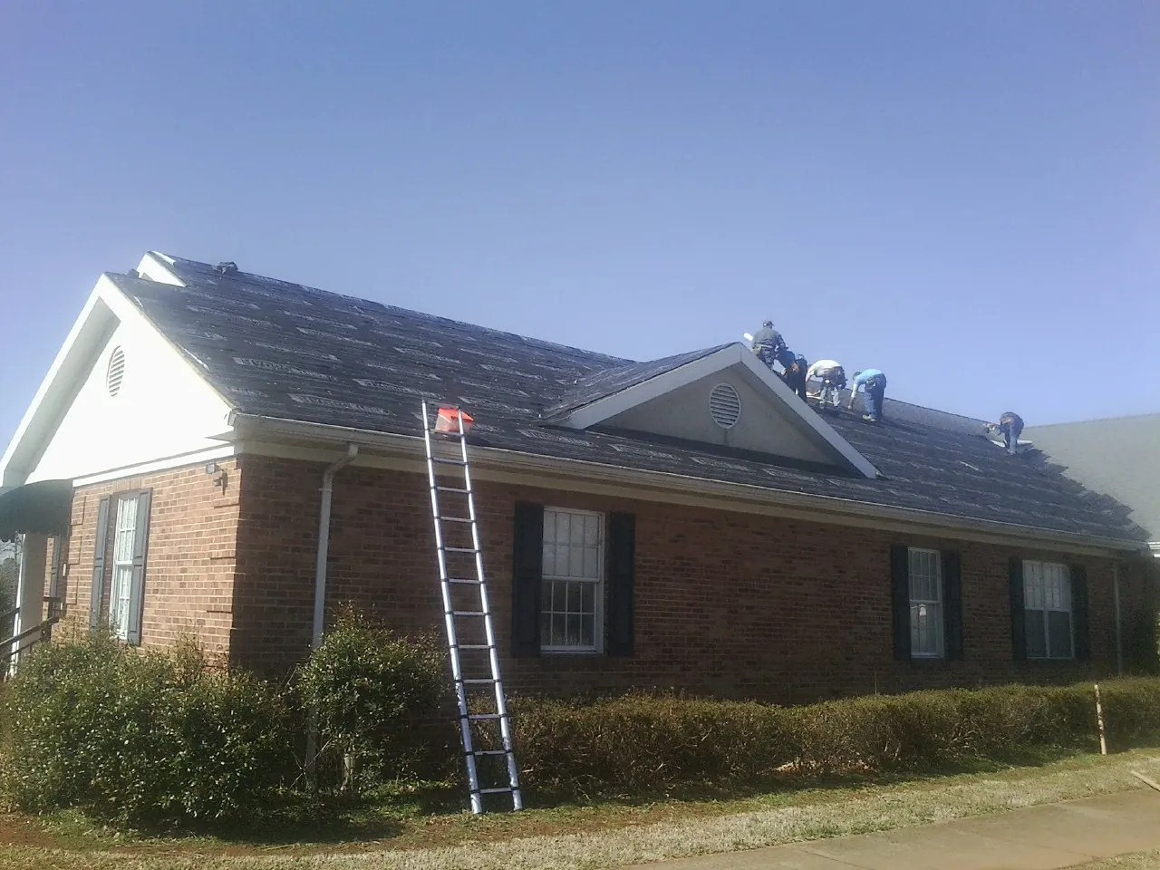 Crew tearing shingles off a brick ranch roof with a ladder set — Metal Roof Repair work by our crew in Coquille