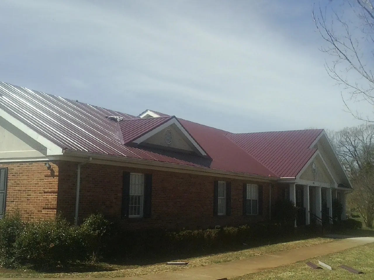 Red metal roof with gabled entries on a long brick building, from a Hail Damage Roof Repair job in Coquille