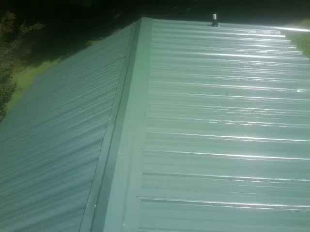 New green metal panels meeting at the ridge of a roof — Flat Roof Repair work by our crew in Coquille