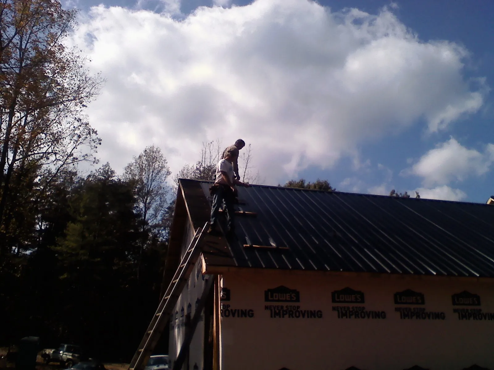 Roofer fastening dark metal panels high against a cloudy sky, from a Roof Inspection job in Coquille