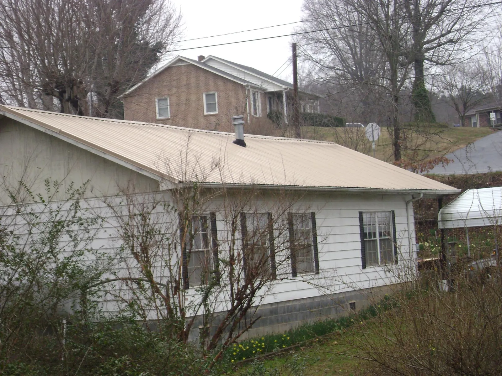 Tan metal roof on a white sided house set into a hillside — Commercial Roofing by Roofing Brothers in Coquille